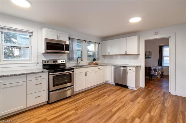 kitchen with sink, white cabinets, stainless steel appliances, a healthy amount of sunlight, and light wood-type flooring