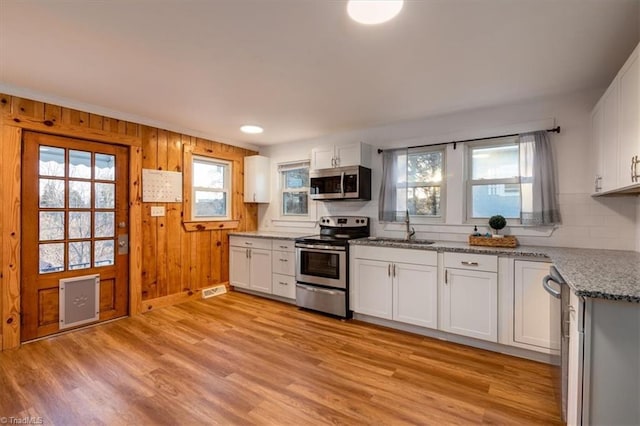 kitchen featuring sink, white cabinets, stainless steel appliances, light stone countertops, and light wood-type flooring