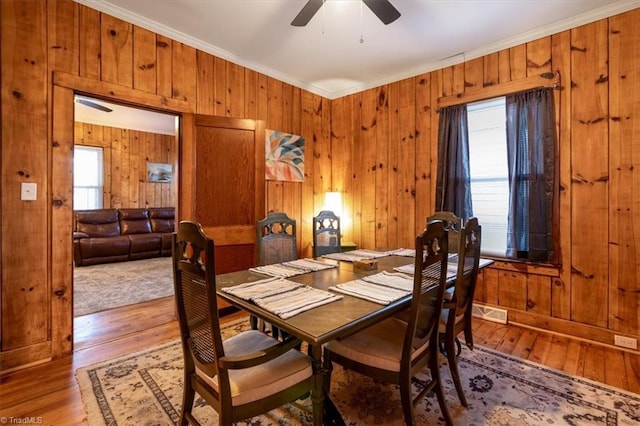 dining space featuring hardwood / wood-style flooring, ceiling fan, ornamental molding, and wooden walls