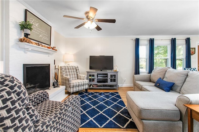 living room with ceiling fan, a large fireplace, wood-type flooring, and crown molding