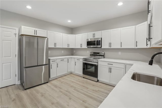 kitchen featuring appliances with stainless steel finishes, light stone counters, sink, light hardwood / wood-style floors, and white cabinetry