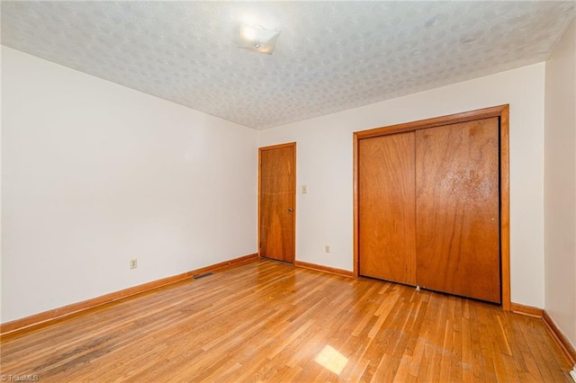 unfurnished bedroom with baseboards, light wood finished floors, visible vents, and a closet