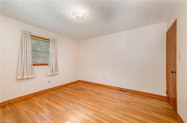empty room featuring baseboards, light wood finished floors, and a textured ceiling