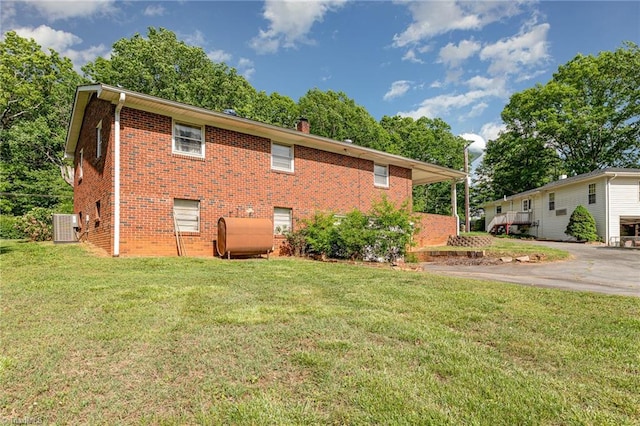 view of home's exterior with central AC, brick siding, heating fuel, a chimney, and a lawn