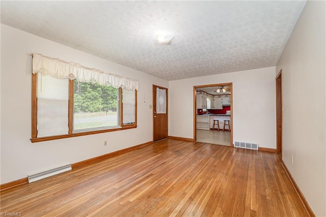 unfurnished room with visible vents, a textured ceiling, light wood finished floors, and baseboards