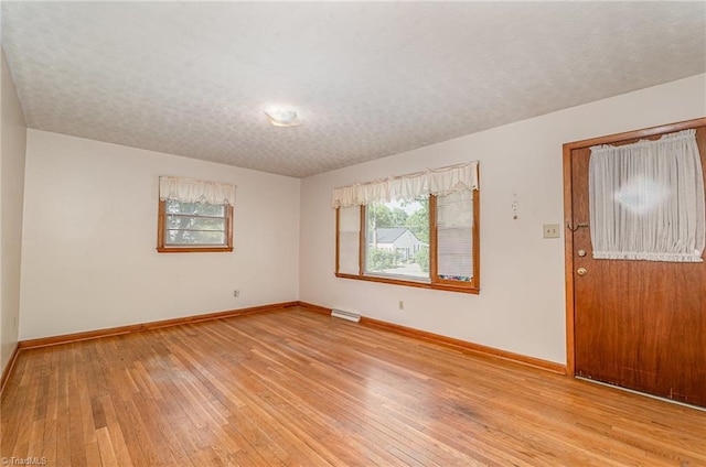 unfurnished room featuring baseboards, a textured ceiling, visible vents, and light wood-style flooring