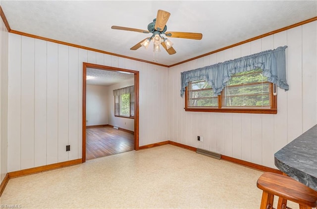 unfurnished room with baseboards, ornamental molding, a ceiling fan, and wood walls