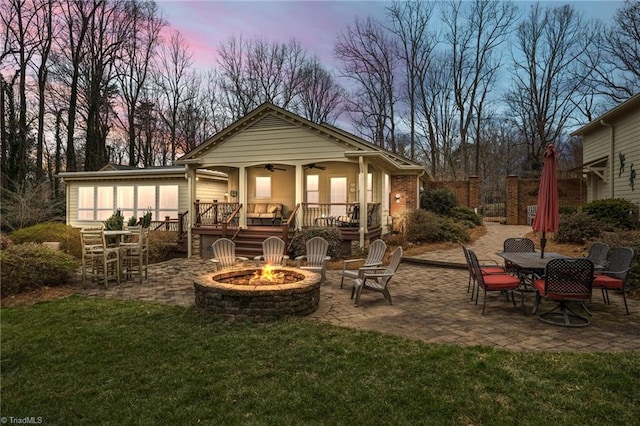 back house at dusk with a patio area, a yard, ceiling fan, and a fire pit