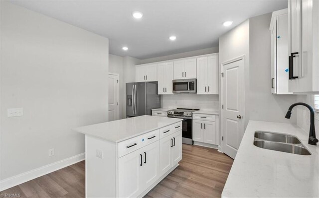 4196 Emmas Way E, Bend, NC 27018 - kitchen with appliances with stainless steel finishes, a sink, light wood-style flooring, a kitchen island, and light countertops
