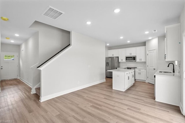 4196 Emmas Way E, Bend, NC 27018 - kitchen featuring appliances with stainless steel finishes, a sink, a center island, white cabinets, and light wood-style flooring