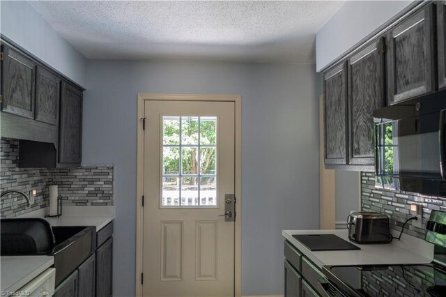 kitchen featuring tasteful backsplash, light countertops, a textured ceiling, a sink, and black microwave
