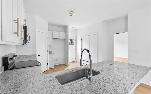 kitchen with range, white cabinets, sink, light stone countertops, and kitchen peninsula