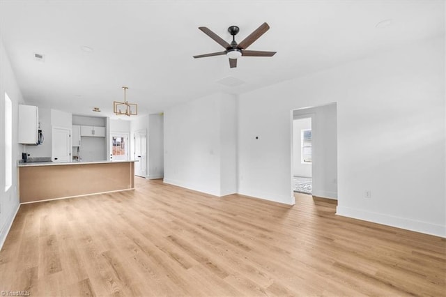 unfurnished living room with ceiling fan with notable chandelier and light wood-type flooring