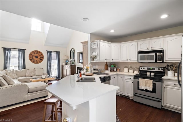 kitchen featuring open floor plan, appliances with stainless steel finishes, a kitchen breakfast bar, a peninsula, and a sink