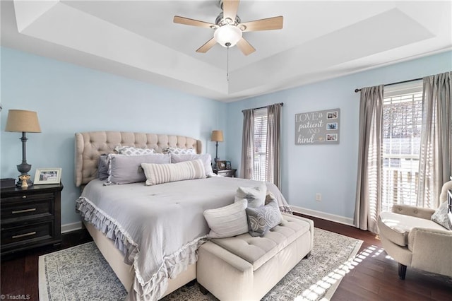 bedroom with dark wood-style floors, multiple windows, a raised ceiling, and baseboards