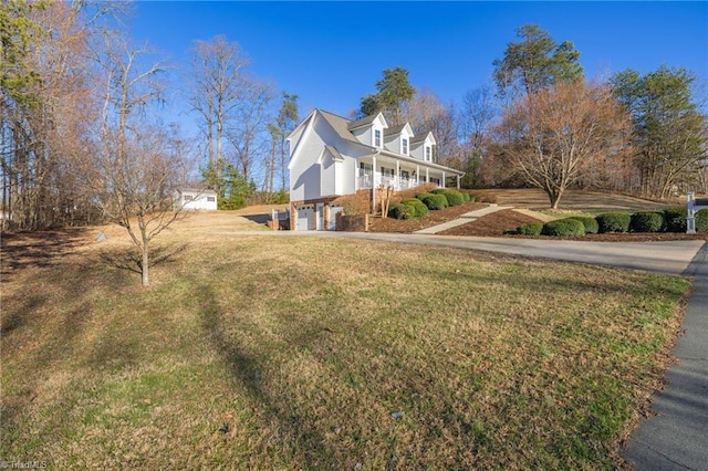 view of side of home with a garage, a lawn, covered porch, and driveway