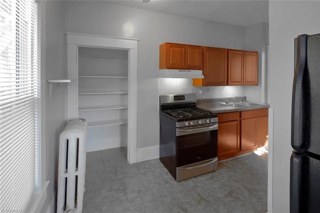 kitchen with under cabinet range hood, a sink, freestanding refrigerator, radiator, and gas range