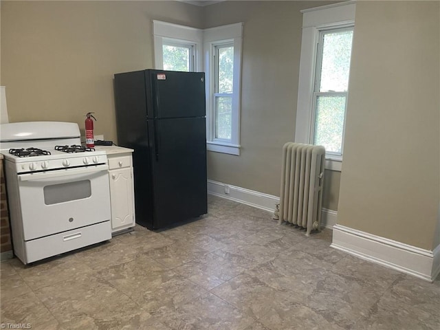 kitchen featuring radiator, freestanding refrigerator, white cabinetry, baseboards, and white gas range oven