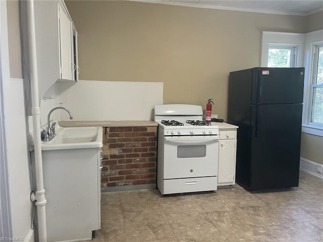 kitchen with white range with gas stovetop, white cabinets, a sink, and freestanding refrigerator