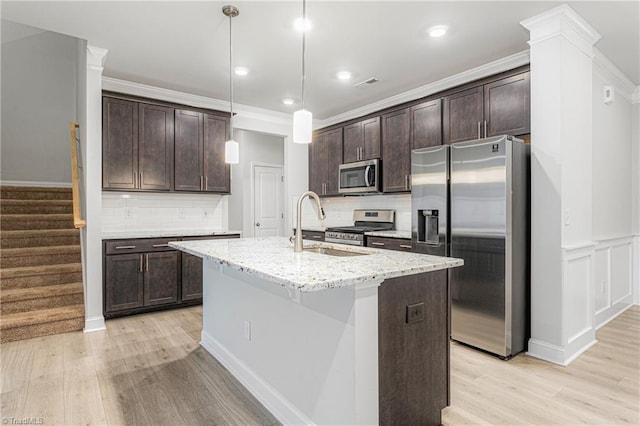 kitchen with stainless steel appliances, dark brown cabinets, a center island with sink, and decorative light fixtures