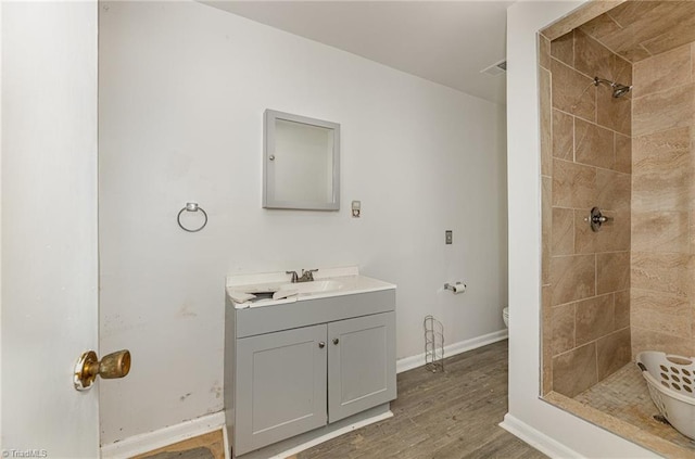 bathroom featuring wood-type flooring, vanity, a tile shower, and toilet