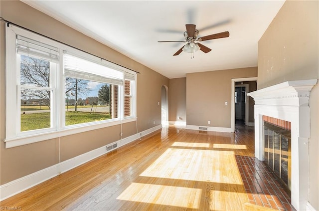 unfurnished living room featuring ceiling fan, wood-type flooring, and a fireplace