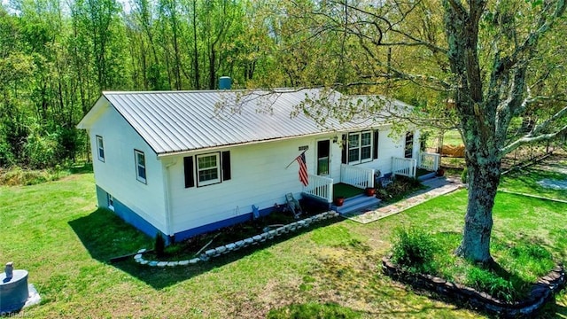 single story home with a front yard, a wooded view, and metal roof