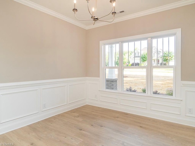 spare room featuring an inviting chandelier, light wood-type flooring, ornamental molding, and a wealth of natural light