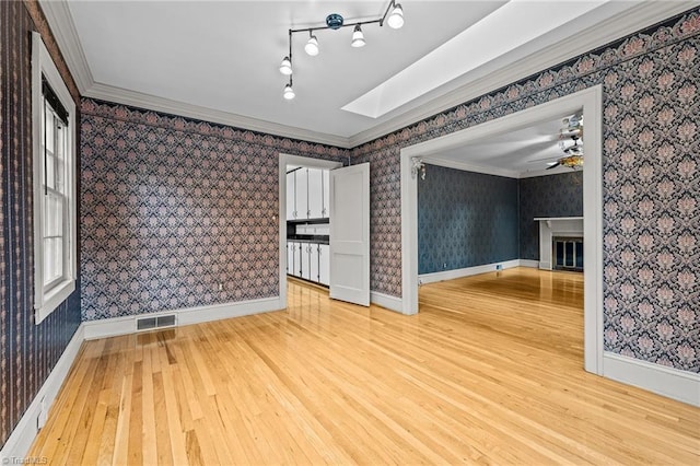 spare room with hardwood / wood-style floors, ceiling fan, a skylight, and ornamental molding