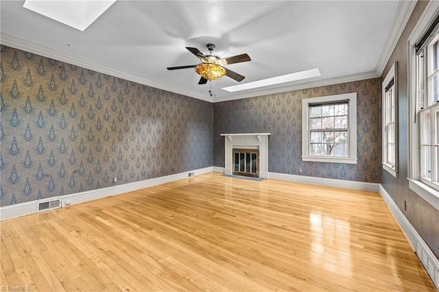 unfurnished living room with light hardwood / wood-style floors, ceiling fan, a skylight, and ornamental molding