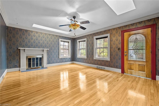 unfurnished living room with ceiling fan, light hardwood / wood-style flooring, a skylight, and ornamental molding