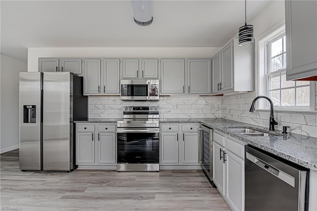 kitchen with sink, stainless steel appliances, wine cooler, pendant lighting, and light hardwood / wood-style floors