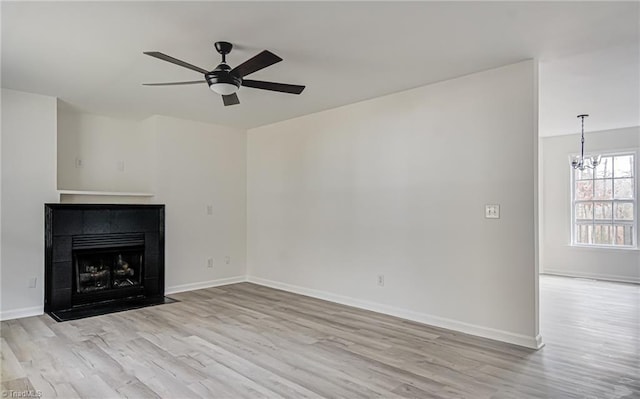 unfurnished living room with ceiling fan with notable chandelier, a tile fireplace, and light hardwood / wood-style flooring