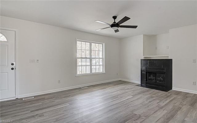 unfurnished living room with a tile fireplace, ceiling fan, and light wood-type flooring