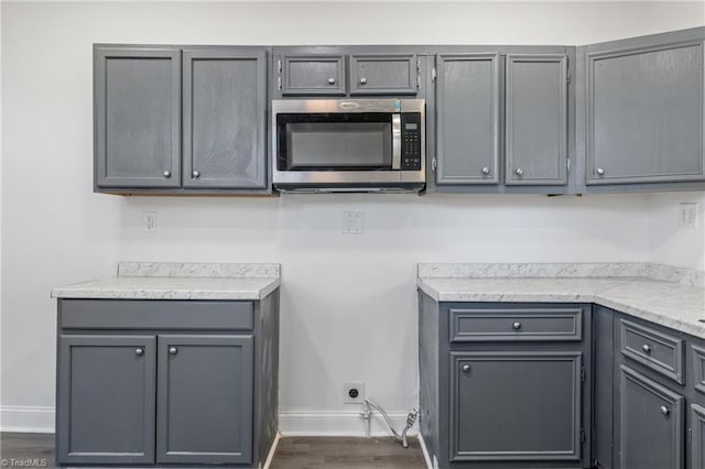 kitchen with gray cabinets, dark wood-type flooring, and light stone countertops