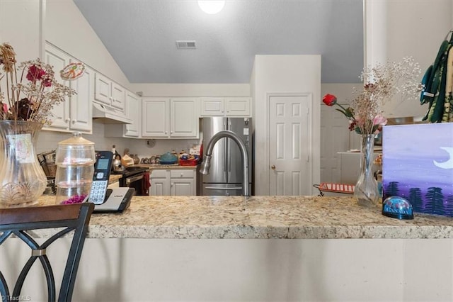 kitchen with under cabinet range hood, visible vents, white cabinetry, light countertops, and freestanding refrigerator