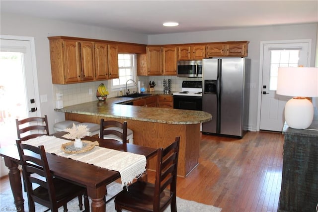 kitchen with appliances with stainless steel finishes, dark wood-type flooring, backsplash, and kitchen peninsula