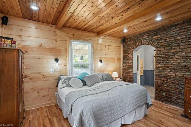 bedroom with light wood-type flooring, beam ceiling, and wooden walls