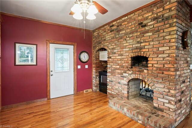 entryway featuring light hardwood / wood-style floors, crown molding, ceiling fan, and a fireplace