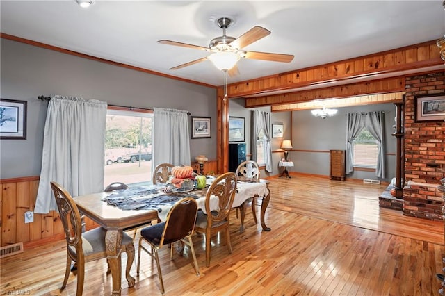 dining space with crown molding, light hardwood / wood-style flooring, ceiling fan with notable chandelier, and wooden walls