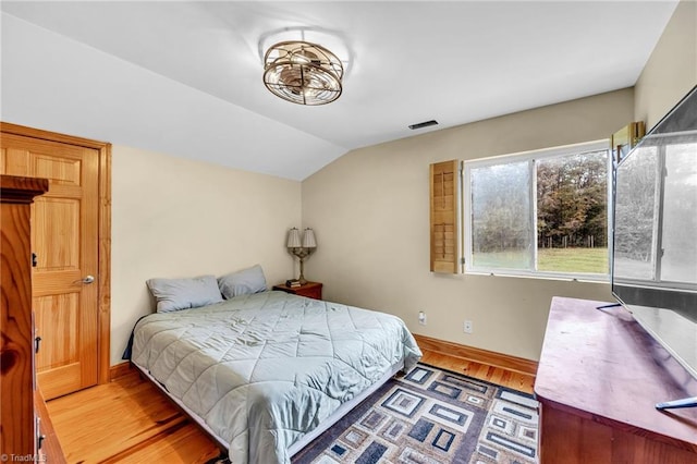 bedroom with baseboards, vaulted ceiling, and wood finished floors