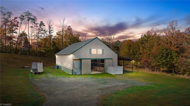 back of property at dusk with a pole building, a detached garage, an outdoor structure, a yard, and driveway