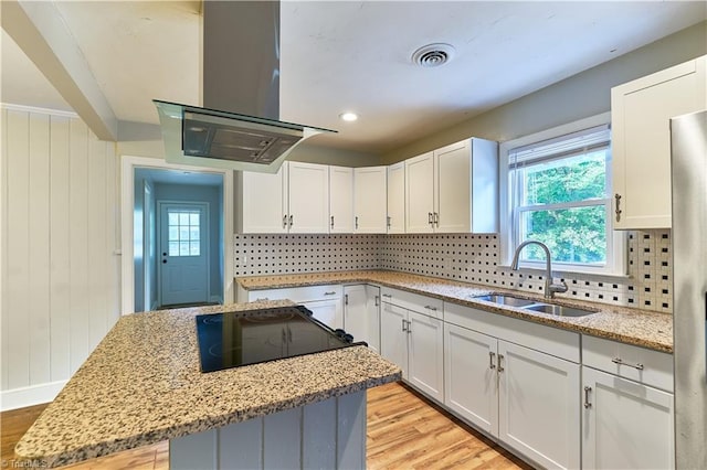 kitchen with a sink, island range hood, stovetop, light wood finished floors, and backsplash