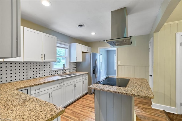 kitchen with island range hood, stovetop, light wood finished floors, a kitchen island, and stainless steel fridge