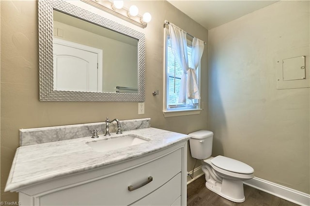 half bath with baseboards, wood finished floors, toilet, and vanity