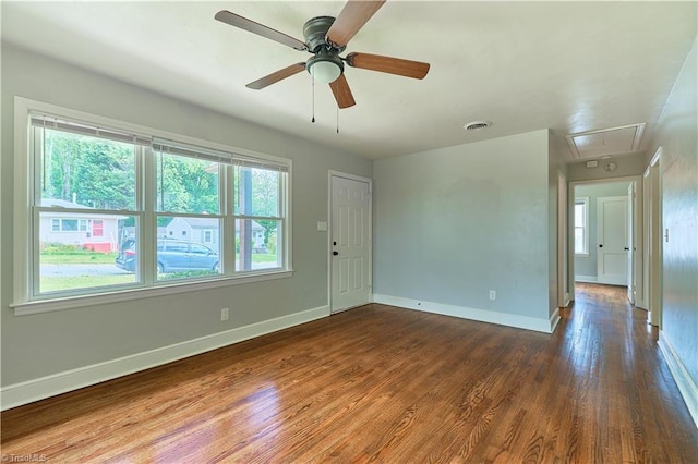 empty room with attic access, wood finished floors, baseboards, and ceiling fan