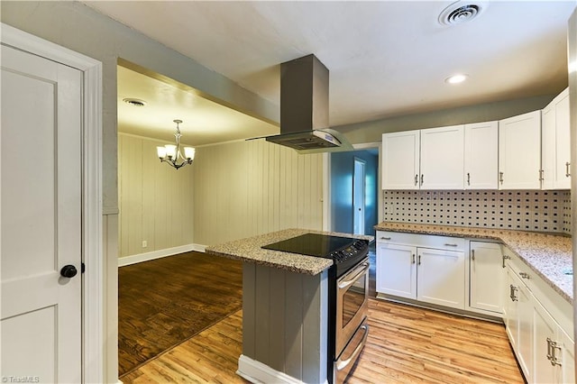 kitchen with stainless steel range with electric stovetop, island range hood, white cabinetry, and a chandelier