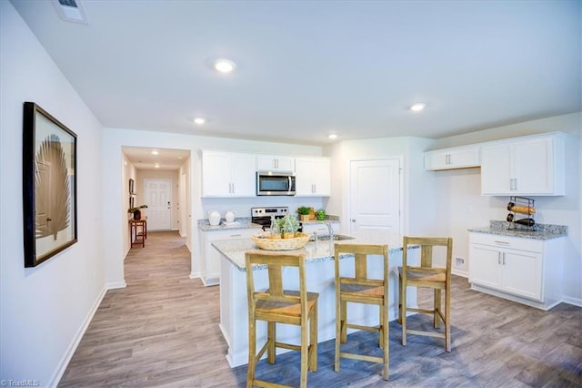 kitchen with light stone countertops, white cabinetry, stainless steel appliances, and light wood-type flooring