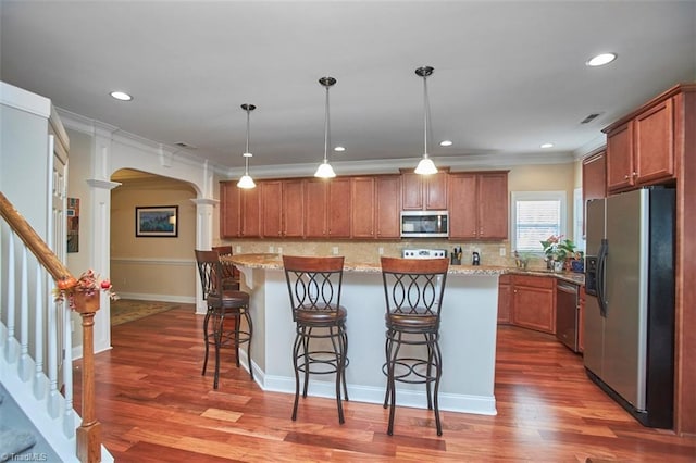 kitchen with a breakfast bar, decorative columns, brown cabinets, appliances with stainless steel finishes, and arched walkways