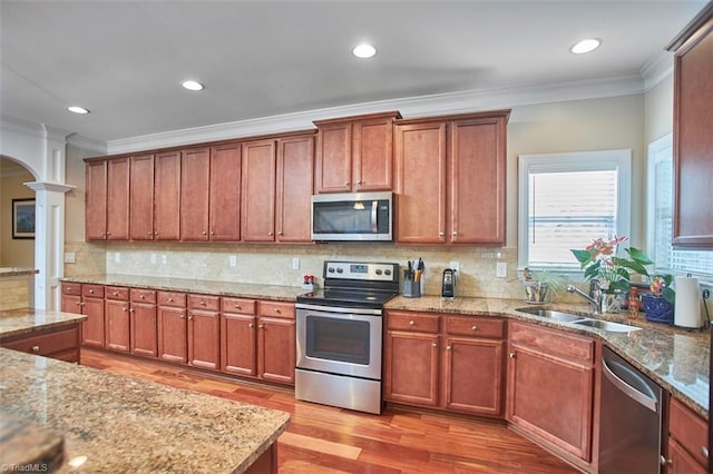 kitchen with ornamental molding, a sink, stainless steel appliances, light wood-style floors, and ornate columns